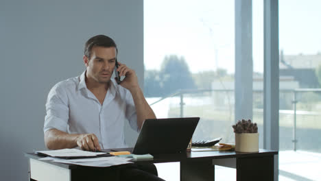 Business-man-working-at-laptop-computer.-Concentrated-man-talking-mobile-phone.