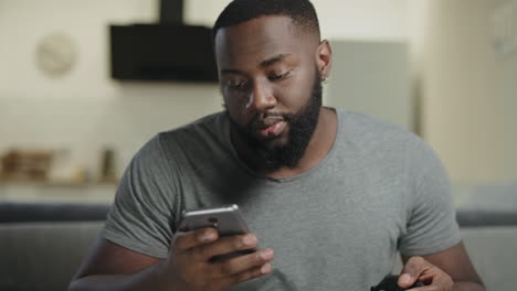 Black-man-holding-phone-at-kitchen.-Closeup-young-adult-texting-in-smartphone.