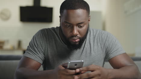 Concentrated-man-sitting-with-phone.-Portrait-of-black-man-typing-message.
