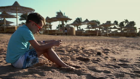 Cute-teenager-playing-mobile-phone-at-seashore.-Young-man-enjoying-sea-at-beach.