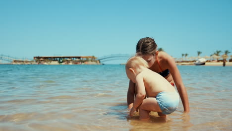 Young-woman-having-fun-with-little-boy-in-warm-water-at-seashore-at-sunny-day.