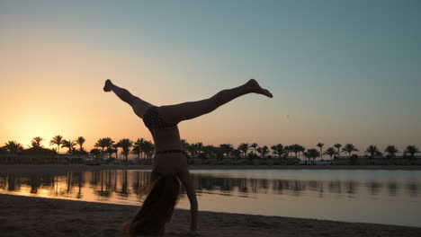 Smiling-young-woman-showing-cartwheel-on-sea-coastline-at-sunset-time.