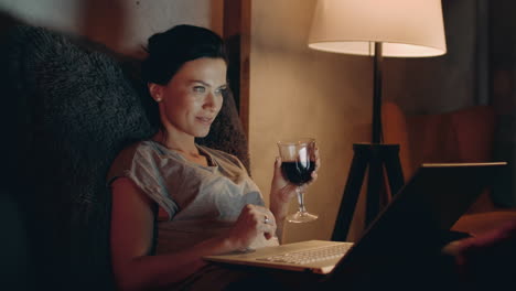 Woman-drinking-red-wine-with-notebook.-Girl-looking-laptop-with-wineglass.