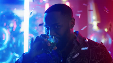 Afro-guy-drinking-alcohol-in-club.-Man-raising-up-glass-on-neon-background.