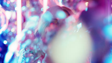 Playful-girl-partying-in-nightclub.-Happy-woman-blowing-confetti-at-disco-party