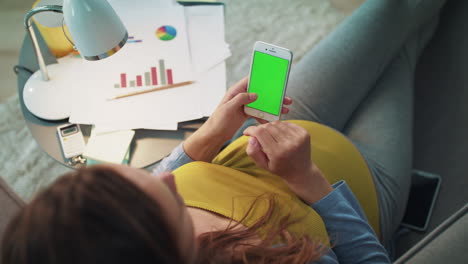 Top-view-of-pregnant-woman-typing-on-smartphone-with-green-screen-at-home.