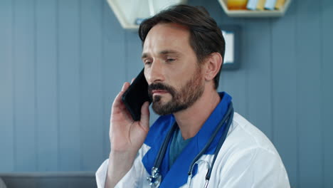 Close-up-tired-male-doctor-talking-phone-in-office.-Doctor-listening-patient