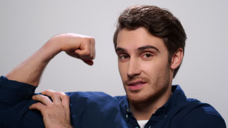 Strong-man-showing-biceps-on-light-background.-Positive-guy-posing-at-camera