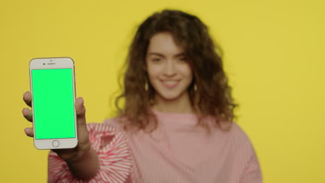 Junge-Frau-Zeigt-Mobiltelefon-Mit-Grünem-Bildschirm-Auf-Gelbem-Hintergrund