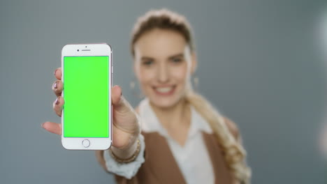 Business-woman-showing-mobile-phone-with-green-screen-in-studio