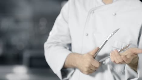 Chef-with-metal-tongs-at-professional-kitchen.-Closeup-male-hands-with-tongs.