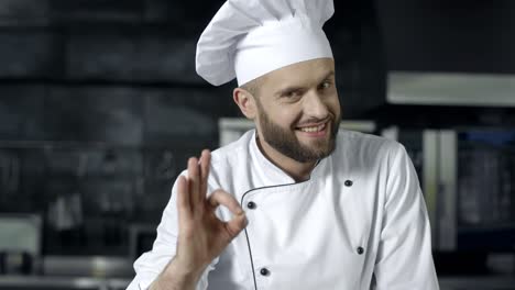 Happy-chef-making-ok-gesture-at-commercial-kitchen.-Chef-man-posing-at-kitchen