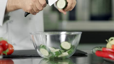 Chef-cutting-fresh-cucumber-in-glass-bowl-in-slow-motion-at-kitchen