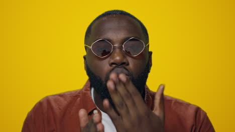 Retrato-De-Un-Apuesto-Hombre-Afro-Enviando-Un-Beso-Aéreo-A-La-Cámara-Sobre-Fondo-Amarillo.