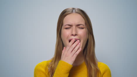 Portrait-of-smiling-woman-yawning-at-camera-on-grey-background-in-studio.