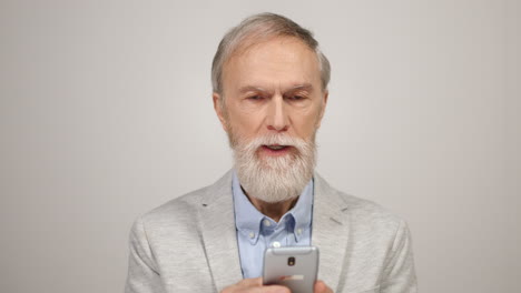 Senior-man-looking-smartphone-indoors.-Focused-gentleman-reading-news-in-studio