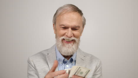 Happy-old-man-counting-money-indoors.-Rich-guy-holding-dollars-in-modern-studio.