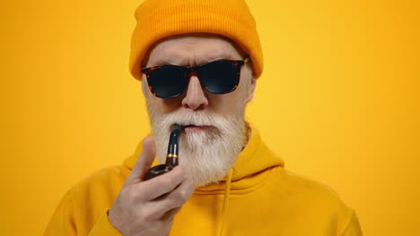Rich-old-man-smoking-pipe-indoors.-Senior-guy-holding-pipe-in-mouth-in-studio.