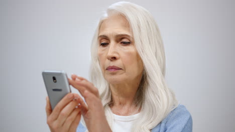 Senior-woman-looking-mobile-phone-indoors.-Old-lady-reading-smartphone-in-studio