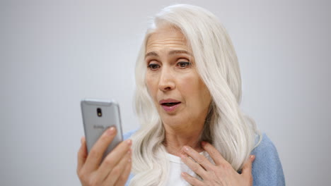 Amazed-woman-saying-wow-indoors.-Old-lady-looking-news-in-smartphone-in-studio.