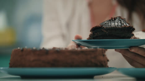 Close-up-of-female-hand-put-sweet-cake-on-plate.-Brown-cake-dessert