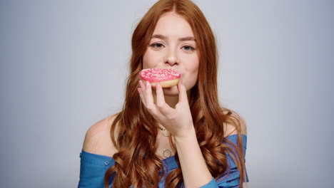 Smiling-woman-eating-doughnut-indoors.-Excited-girl-having-snack-in-studio