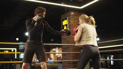 Friendly-trainer-teaching-fit-girl-on-boxing-ring.-Opponents-boxing-at-gym