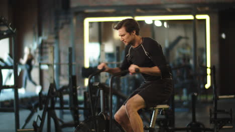 Eager-athlete-doing-cardio-in-sport-club.-Fit-man-training-on-exercycle-at-gym
