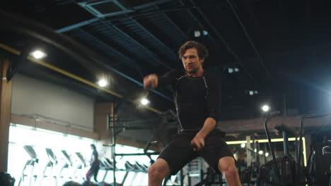 Focused-bodybuilder-using-battle-ropes-in-sport-club.-Athlete-exercising-at-gym