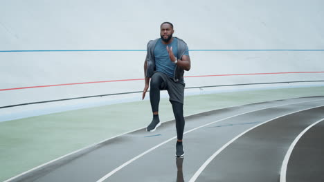 Sportsman-doing-high-knee-taps-during-workout.-Guy-training-on-stadium-track