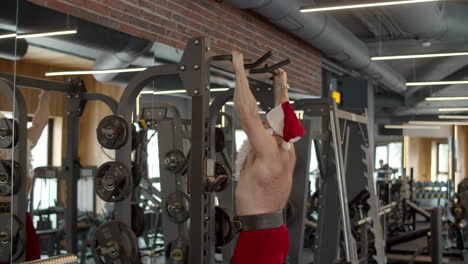 Ambitious-santa-man-having-workout-in-fitness-center.-Sportsman-doing-pullups