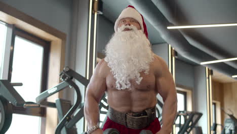 Santa-claus-training-in-sport-club.-Sexy-santa-doing-dumbbell-swings-at-gym.