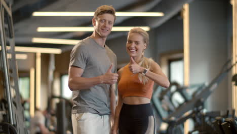 Winners-couple-showing-like-signs-in-sport-club.-Couple-enjoying-results-at-gym