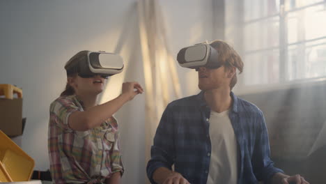 Focused-couple-in-vr-glasses-moving-hands-indoors.-Home-renovation-concept.