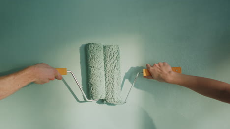 Unknown-couple-doing-decoration-work-in-home.-People-pushing-rollers-on-wall.
