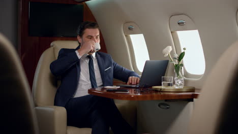 Finance-manager-take-sip-of-coffee-on-business-trip.-Confident-boss-work-laptop