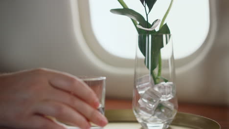 Hand-Stellt-Wasserglas-Auf-Den-Tisch,-Nahaufnahme.-Flugzeugpassagier,-Der-Sich-Auf-Der-Reise-Ausruht