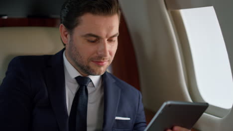 Successful-manager-tapping-tablet-in-plane-closeup.-Focused-ceo-using-computer