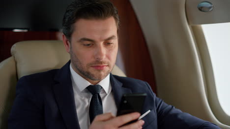 Hübscher-Unternehmer,-Der-Sein-Smartphone-Im-Flugzeug-Verwendet,-Nahaufnahme.-Erfolgreiche-CEO-Reise