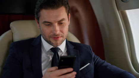 Successful-man-looking-smartphone-at-airplane-window.-Delighted-businessman-rest