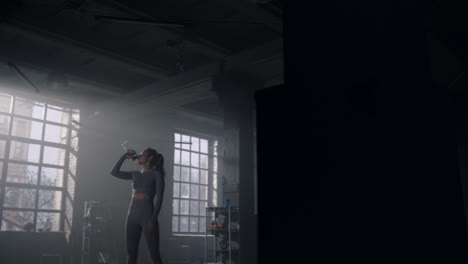 Woman-standing-in-gym-with-water-bottle.-Girl-drinking-water-from-bottle