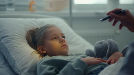 Sad-girl-lying-hospital-bed-hug-toy-portrait.-Doctor-checking-patient-symptoms