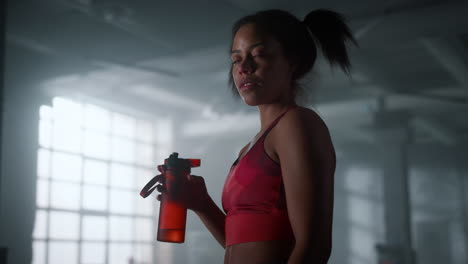 Tired-sportswoman-with-water-bottle-standing-in-gym.-Woman-taking-break