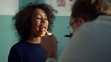 Doctor-using-depressor-checking-girl-throat-closeup.-Medic-looking-in-open-mouth
