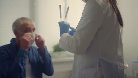 Woman-medic-taking-saliva-sample-old-patient.-Doctor-testing-senior-man-on-covid
