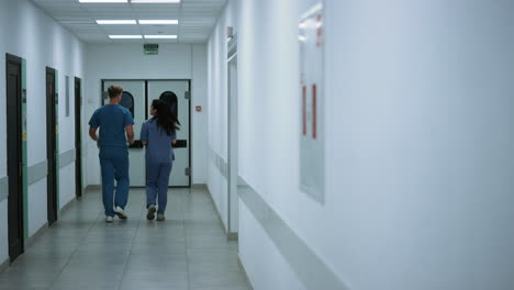 Unknown-doctor-nurse-moving-down-hallway-back-view.-Surgeon-consulting-woman.