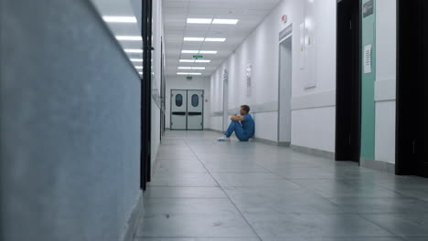 Professional-medic-resting-alone-in-hospital-corridor.-Surgeon-sitting-on-floor.