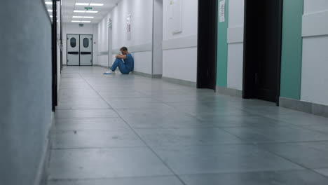 Tired-doctor-sitting-hospital-corridor-floor.-Overwhelmed-surgeon-resting-alone.