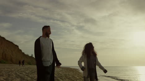 Playful-couple-walking-beach-sunset-sea-sky.-Lovers-enjoy-hold-hands-on-coast.