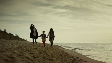 Family-hold-hands-beach-by-sunset-sea.-Mom-dad-child-running-sand-on-holiday.